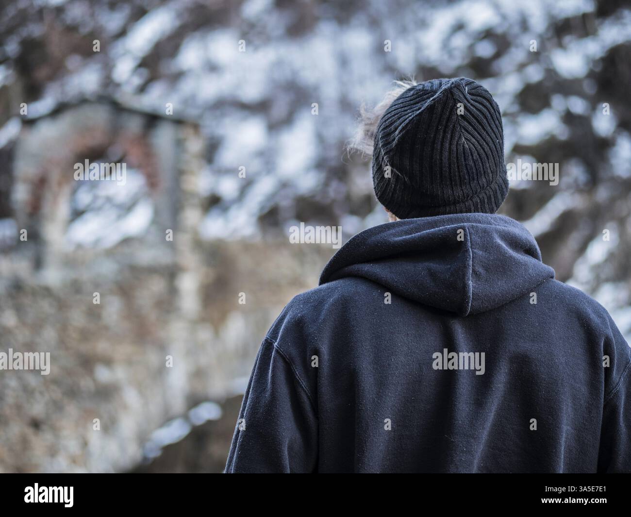 Der Rücken eines jungen Mannes im Hoodie posiert im Winter im Freien mit Schnee herum, nicht erkennbar Stockfoto