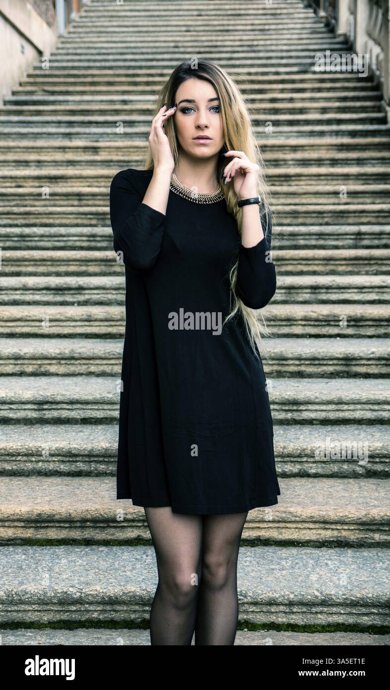Porträt von attraktive blonde junge Frau im schwarzen Kleid, im freien Blick in die Kamera, auf großen alten Steintreppen Stockfoto