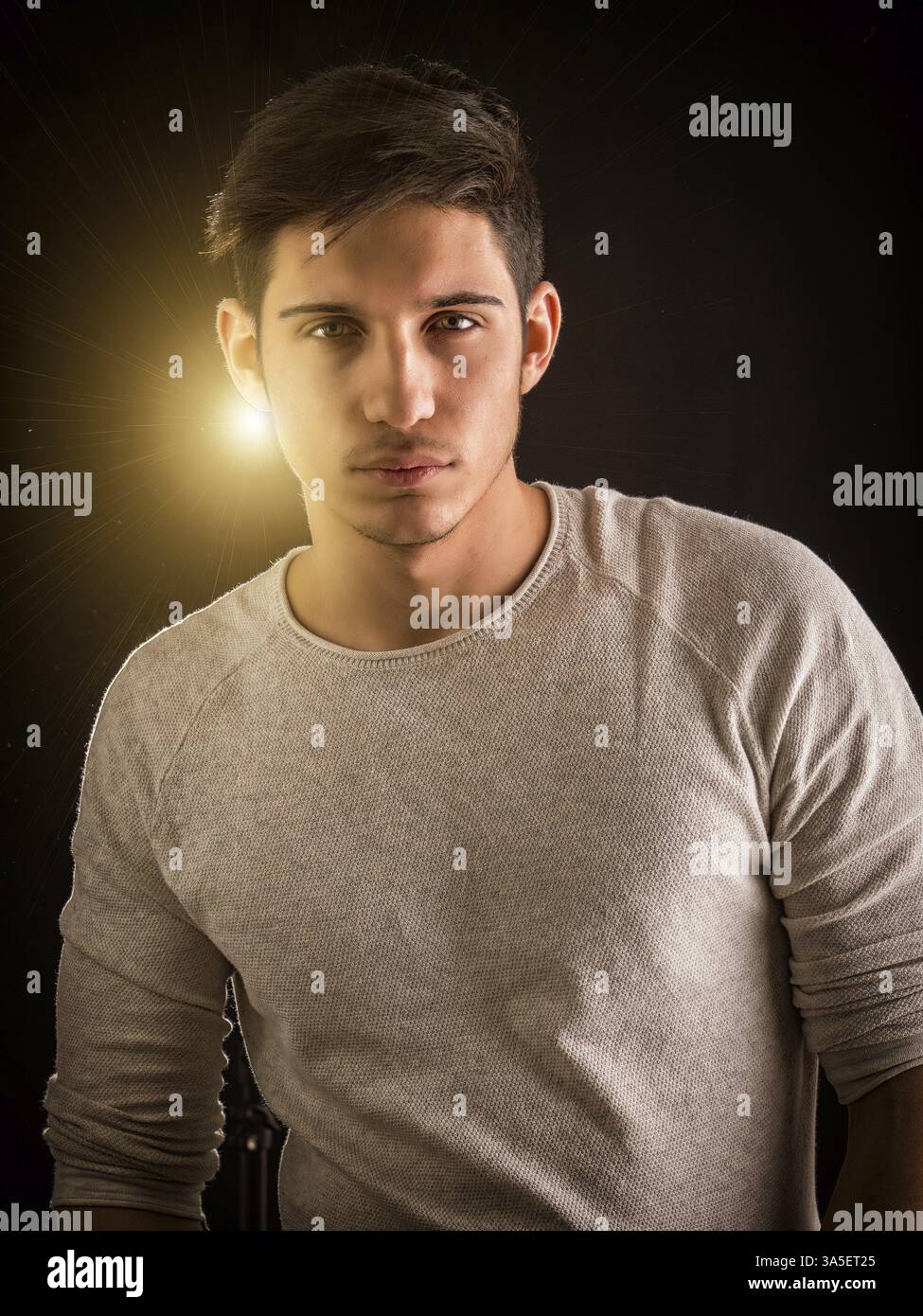 Ein hübscher junger Mann, der selbstbewusst in legerer Kleidung steht, die Kamera anschaut und hinter ihm das Licht leuchtet Stockfoto