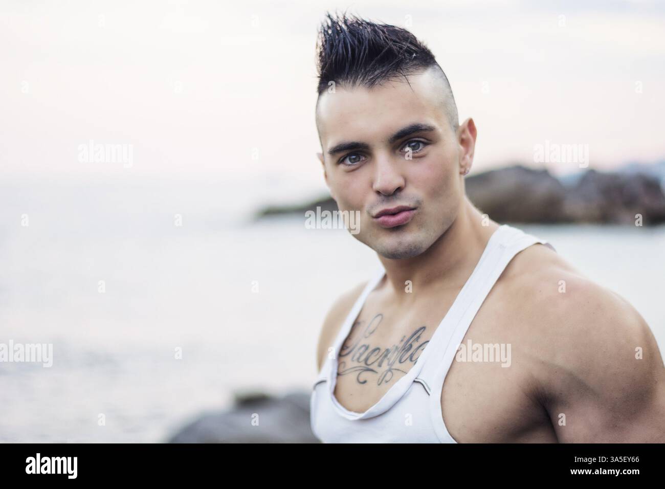 Dreiviertelaufnahme eines gutaussehenden athletischen Mannes in trendiger Kleidung, der mit durchdachtem Gesichtsausdruck vor dem Hintergrund des Himmels aufblickt Stockfoto