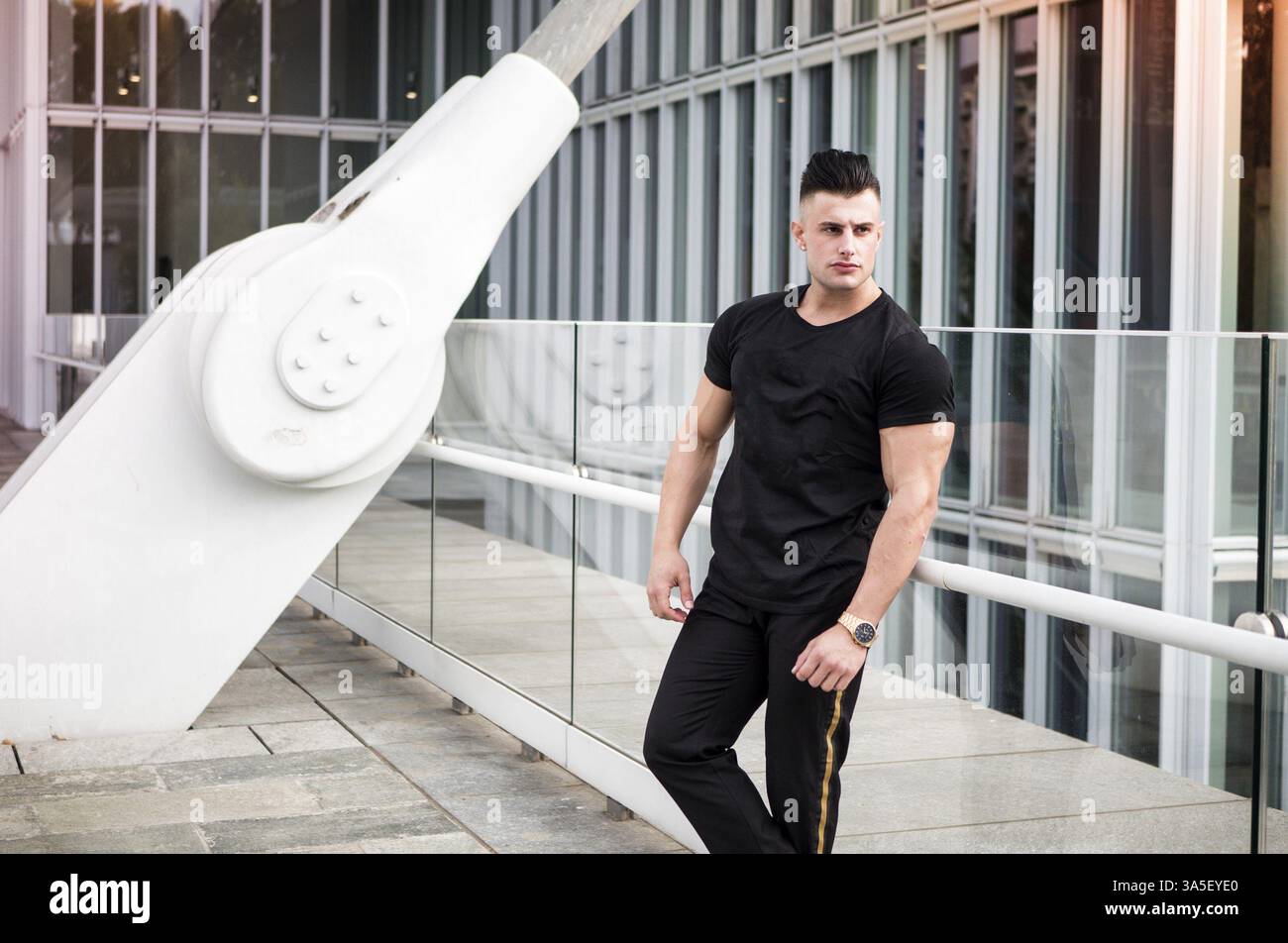 Ein hübscher, lässiger junger Mann in einer modernen, urbanen Umgebung in der europäischen Stadt, stehend und in die Kamera schaut Stockfoto