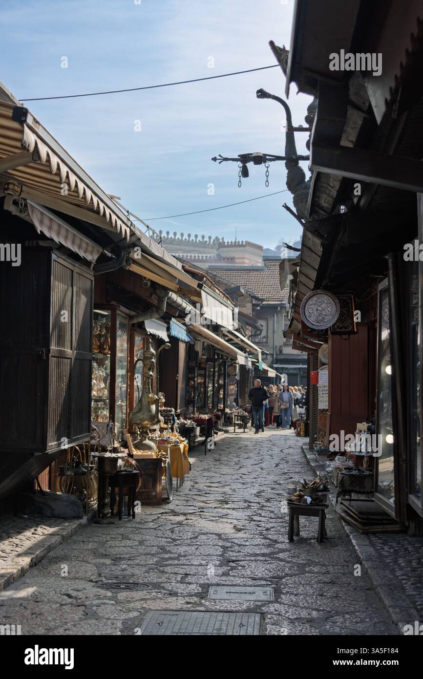Einkaufsmöglichkeiten in der Kazandžiluk-Straße - oder Kupferschmiedegasse - in der historischen osmanischen Altstadt von Sarajevo an einem sonnigen Tag und Souvenirs vor den Geschäften. Stockfoto