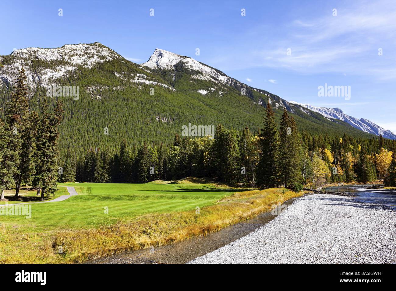 Die Rocky Mountains von Kanada. Golfplätze am Fuße der Rundle und der Cascade Mountains. Flacher Bach mit Kiesboden. Sonniger Tag im Herbst Stockfoto