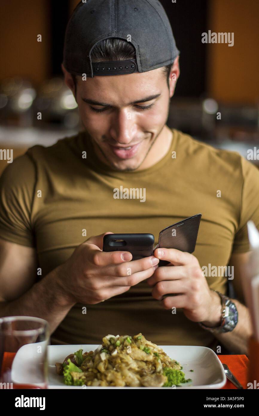Seitenansicht eines hübschen jungen Mannes, der ein Foto von seinem Essen im Restaurant macht. Vertikale Innenaufnahme Stockfoto
