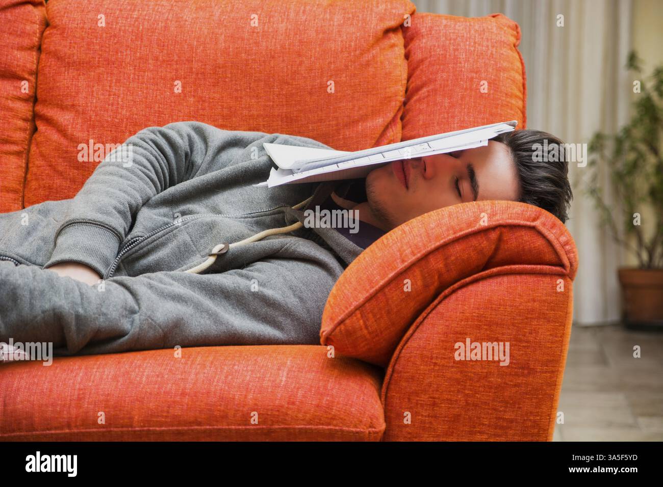 Über-arbeitete, müde Junge Mann zu Hause schlafen anstatt zu arbeiten oder studieren, ruht mit Kopf von Papier abgedeckt Stockfoto