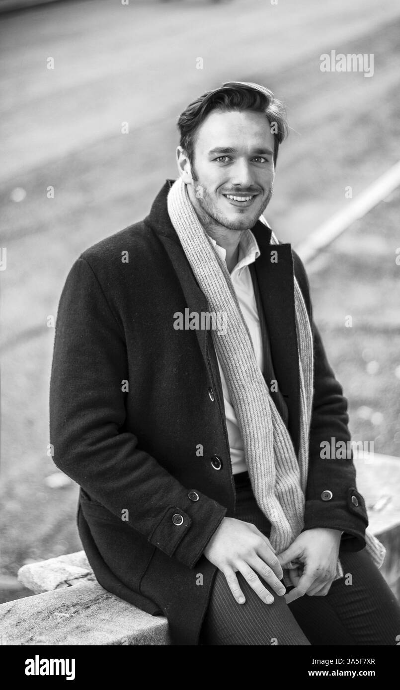 Hübscher junger Mann outdoor im Wintermode tragen schwarzer Mantel und Schal im Stadtpark Stockfoto
