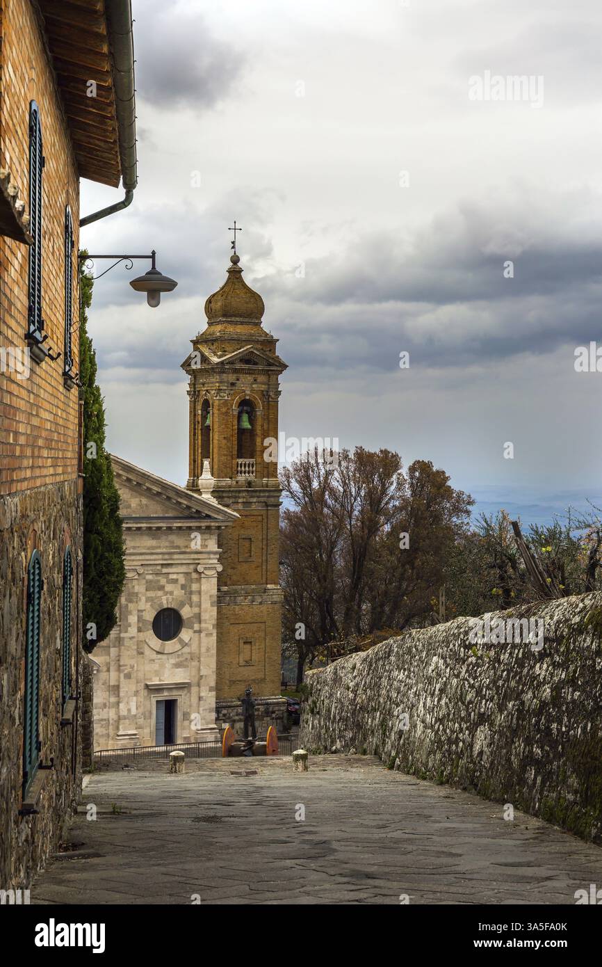 Die Fassade und der Glockenturm der Kirche. Wolkiger Herbsttag in der Toskana. Die kleine Stadt Montalcino. Das Konzept der kognitiven, aktiven und Foto-Touris Stockfoto
