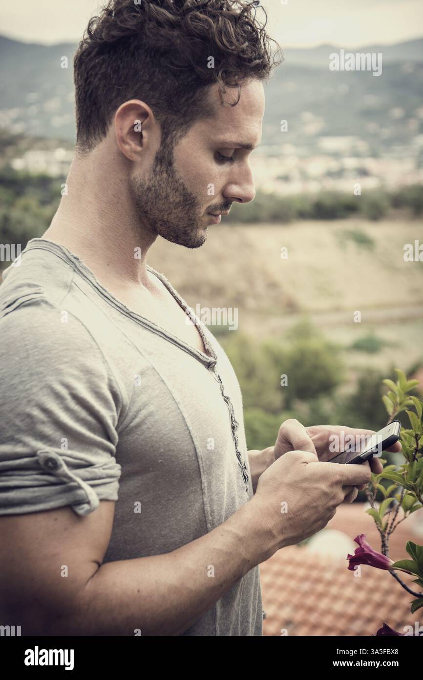 Hübscher trendigen Mann mit Handy Typ SMS im Freien. Seitenansicht Stockfoto