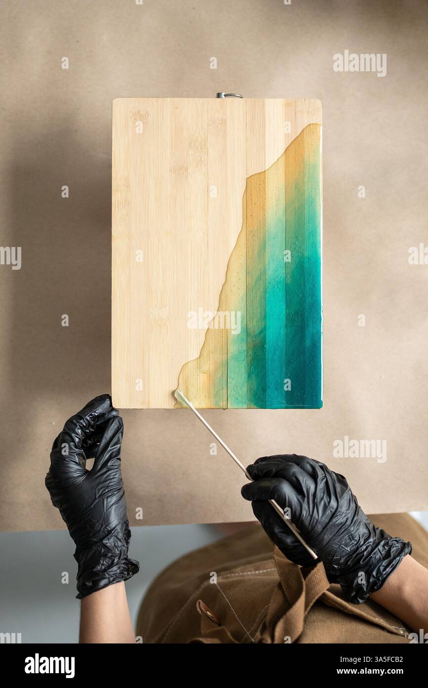 Hände von Künstlern arbeiten mit an Bord verteilten Epoxidharzpigmenten. Komplizierter Konstruktionsverlauf. Draufsicht Stockfoto