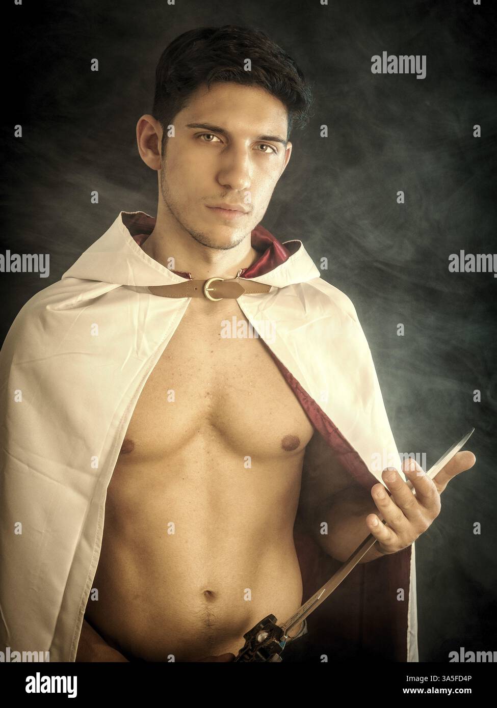 Hübscher junger Mann in altmodischem Mantel mit Schwert auf dunklem rauchigen Hintergrund Stockfoto