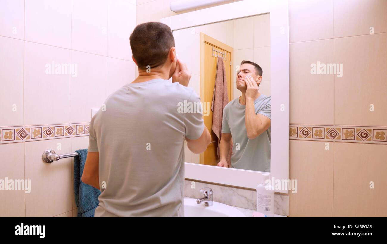 Mann übt Gesichtsreinigungsroutine im modernen Badezimmer Stockfoto