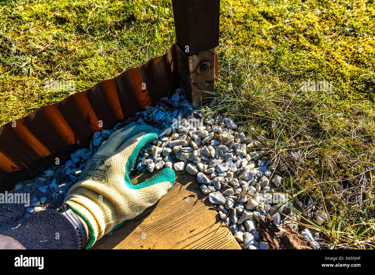 Dekorieren der Terrasse im Garten, Ausgießen kleiner weißer dekorativer Steine auf der Veranda im Garten, einen Eimer mit Steinen zur Dekoration Stockfoto
