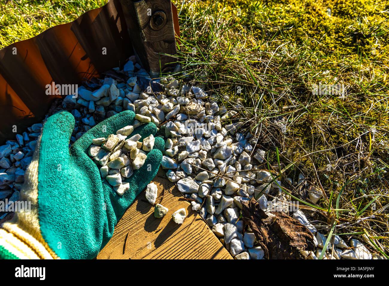 Dekorieren der Terrasse im Garten, Ausgießen kleiner weißer dekorativer Steine auf der Veranda im Garten, einen Eimer mit Steinen zur Dekoration Stockfoto