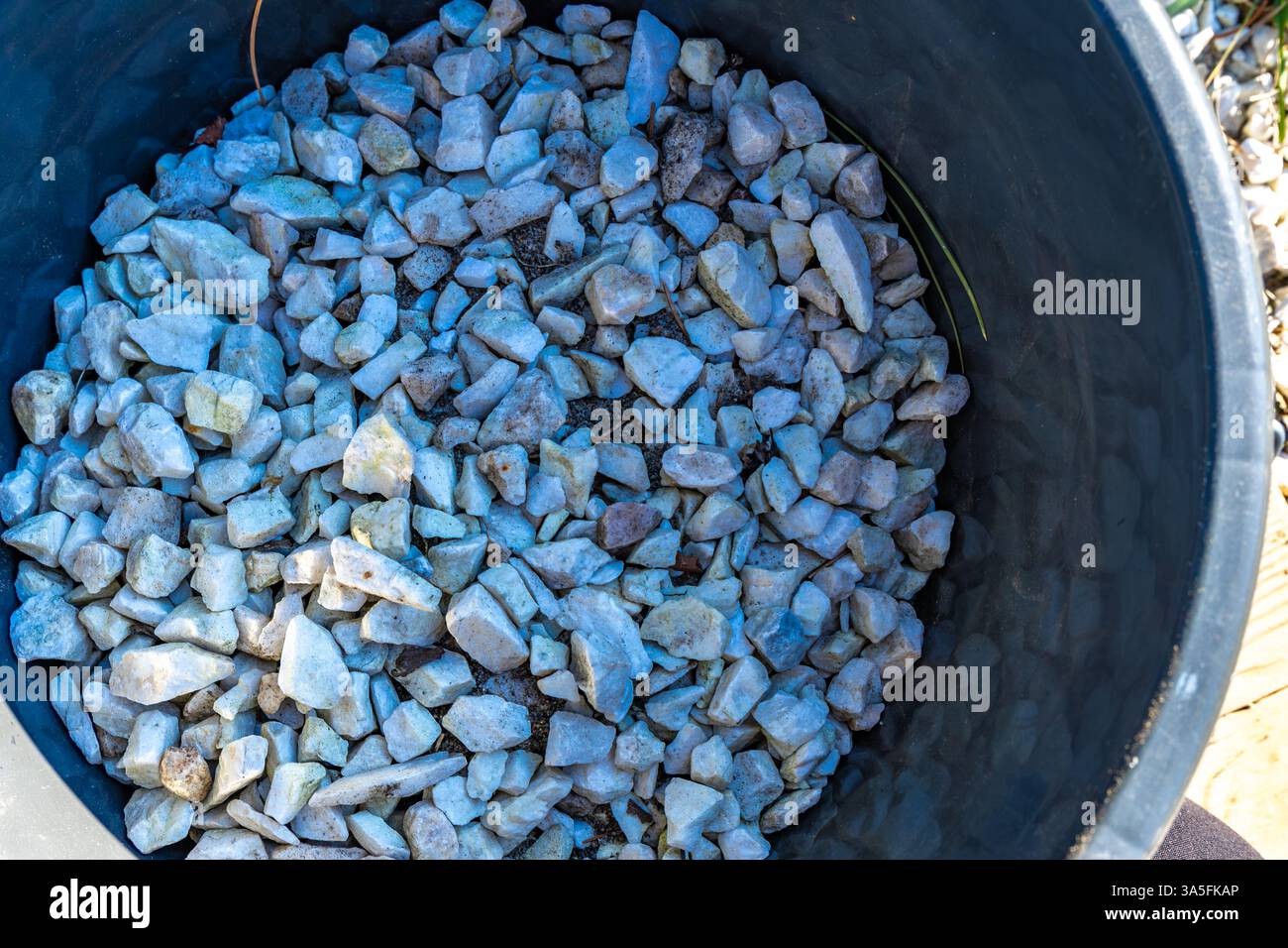 Dekorieren der Terrasse im Garten, Ausgießen kleiner weißer dekorativer Steine auf der Veranda im Garten, einen Eimer mit Steinen zur Dekoration Stockfoto