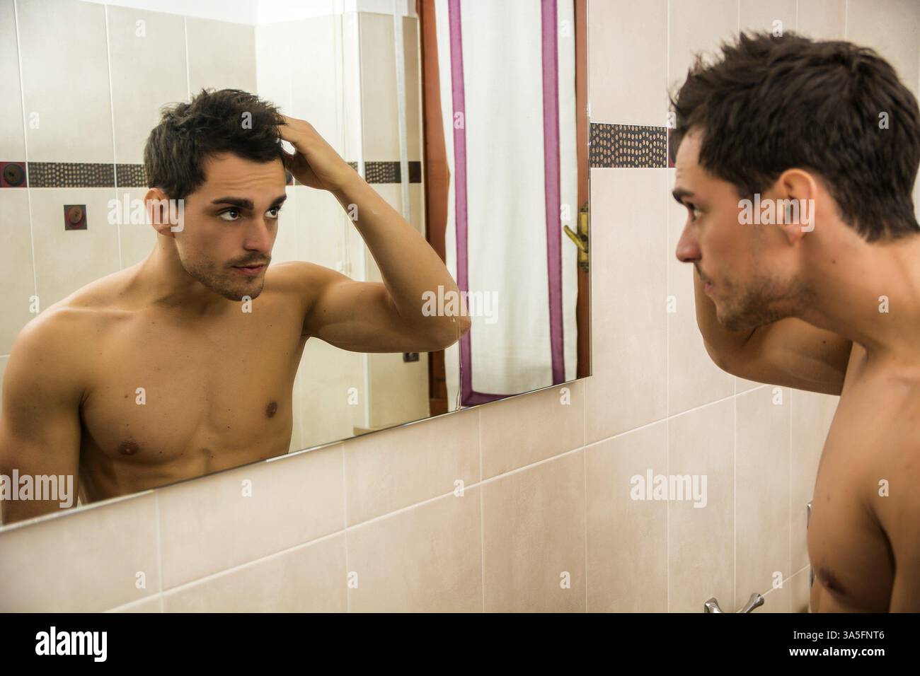 Gut aussehender Mann Blick auf sein Gesicht im Spiegel, Überprüfung von Haar und Haaransatz Stockfoto