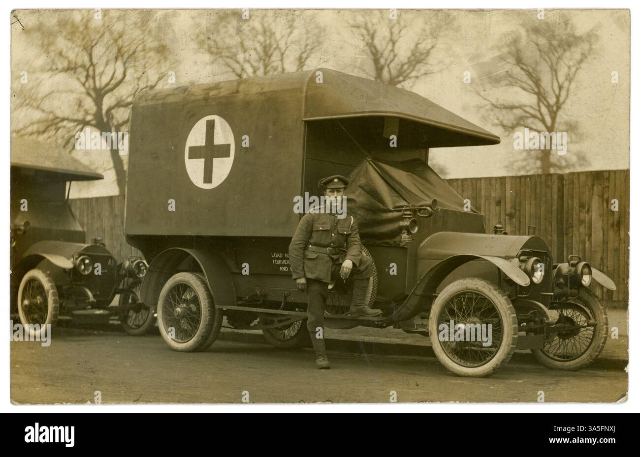 Ursprünglicher britischer Krankenwagenfahrer aus dem 1. Weltkrieg, Army Service Corps (ASC)-Kappenabzeichen, ein Schlüsselband auf seiner Schulter, neben der Kabine seines Krankenwagens, einer aus einer Flotte von Krankenwagen, rotes Kreuz auf der Seite. Der junge Mann hat vielleicht an einer der Motorenprüfschulen in London oder Glasgow ausgebildet. Soldaten des Ersten Weltkriegs. Britische Postkarte, 1914-1918. Stockfoto