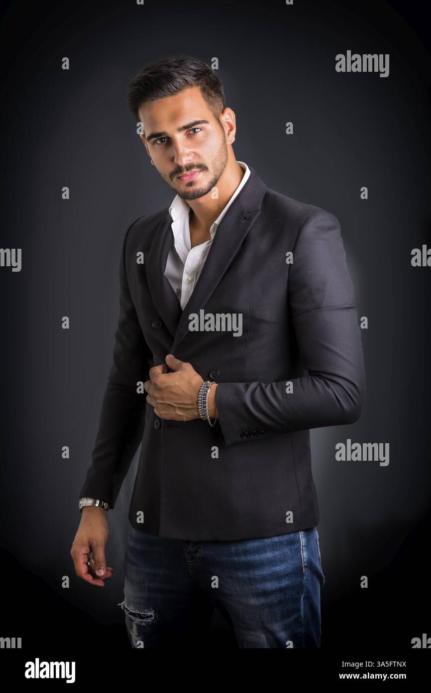 Junger Geschäftsmann zuversichtlich posieren vor der Kamera, tragen Business-Anzug ohne Krawatte mit Hemd am Hals, geöffnet auf dunklem Hintergrund Stockfoto