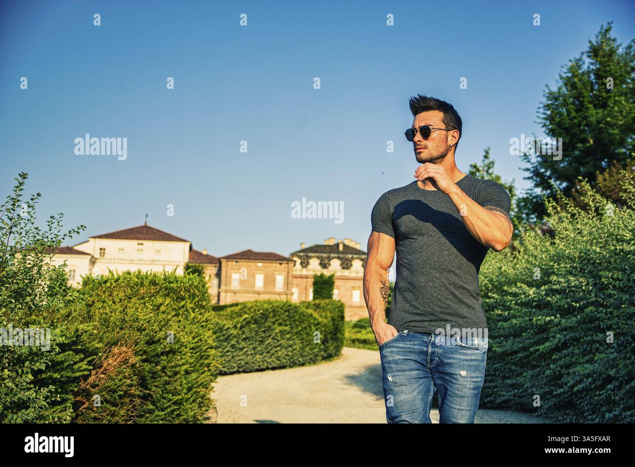 Ein Mann, der auf einem Feldweg steht, mit Bäumen im Hintergrund. Foto eines Mannes, der auf einer unbefestigten Straße steht, umgeben von Bäumen Stockfoto