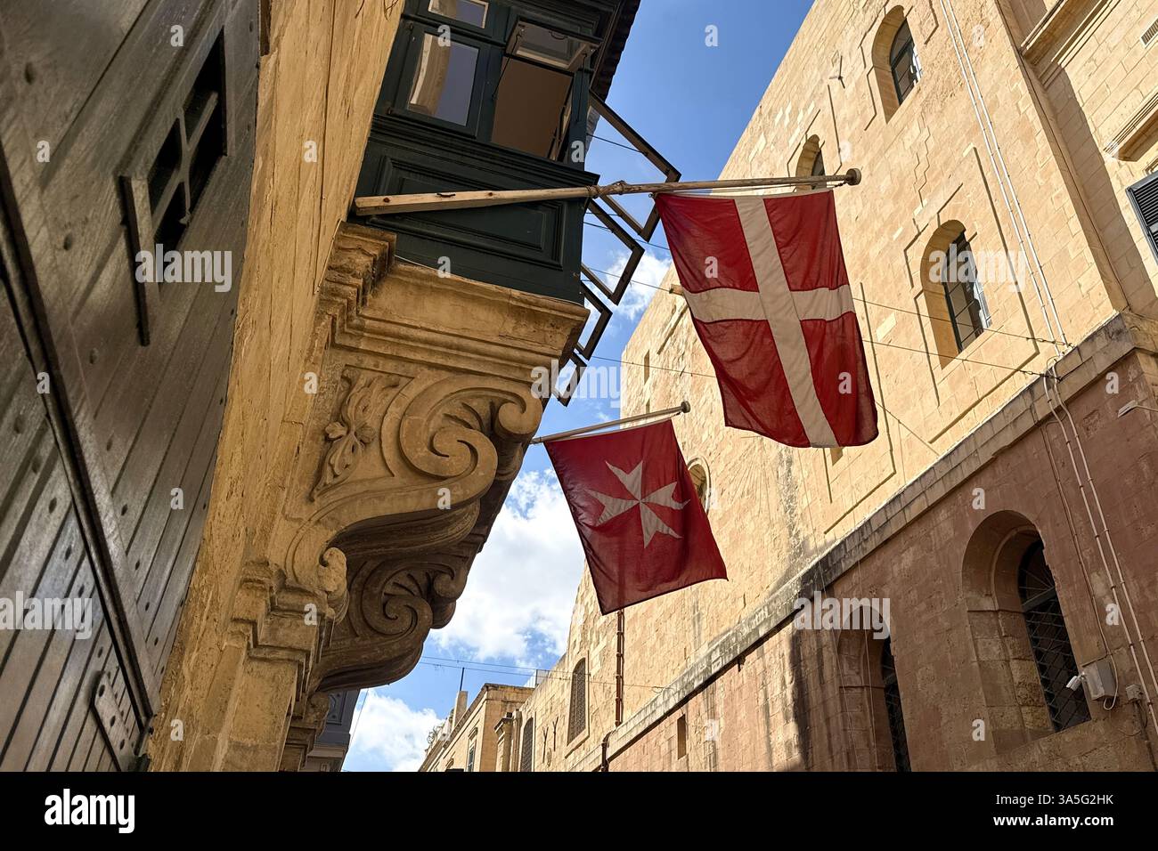 Maltas einzigartiger architektonischer Stil und Symbolik: Enge Gassen der Altstadt mit hervorstehenden Balkonen, wo die Flaggen des Malteserordens stehen Stockfoto