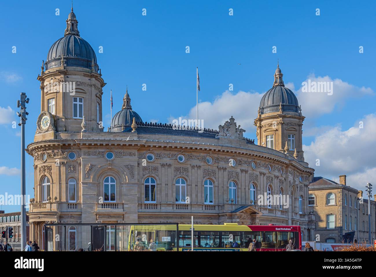 Ein aufwändiges geschwungenes Gebäude aus dem 19. Jahrhundert in einem Stadtzentrum. Im Vordergrund befindet sich ein Bus und ein Himmel mit Wolken. Stockfoto
