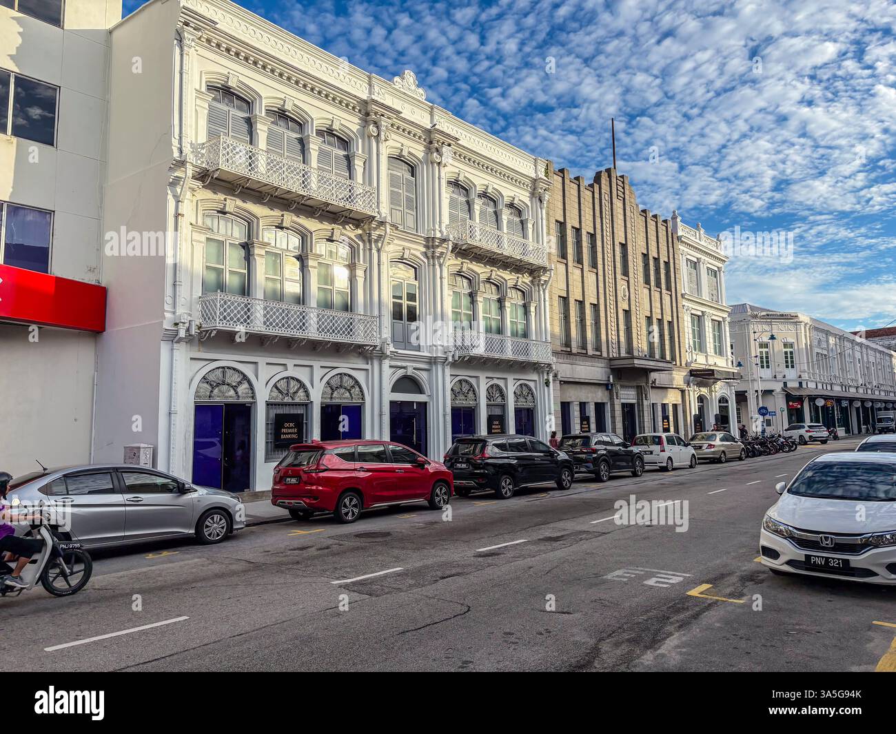 Historische Gebäude entlang einer Straße in George Town, Penang, Malaysia. Eine Reihe von Autos am Straßenrand. Stockfoto