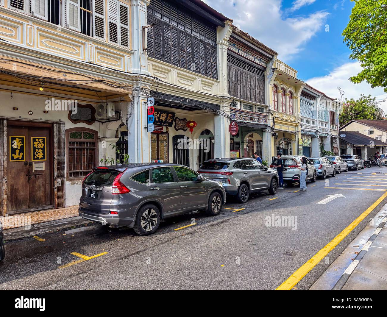 An einem bewölkten Tag säumen geparkte Autos eine Straße mit Ladenhäusern aus der Kolonialzeit in George Town, Penang, Malaysia. Stockfoto