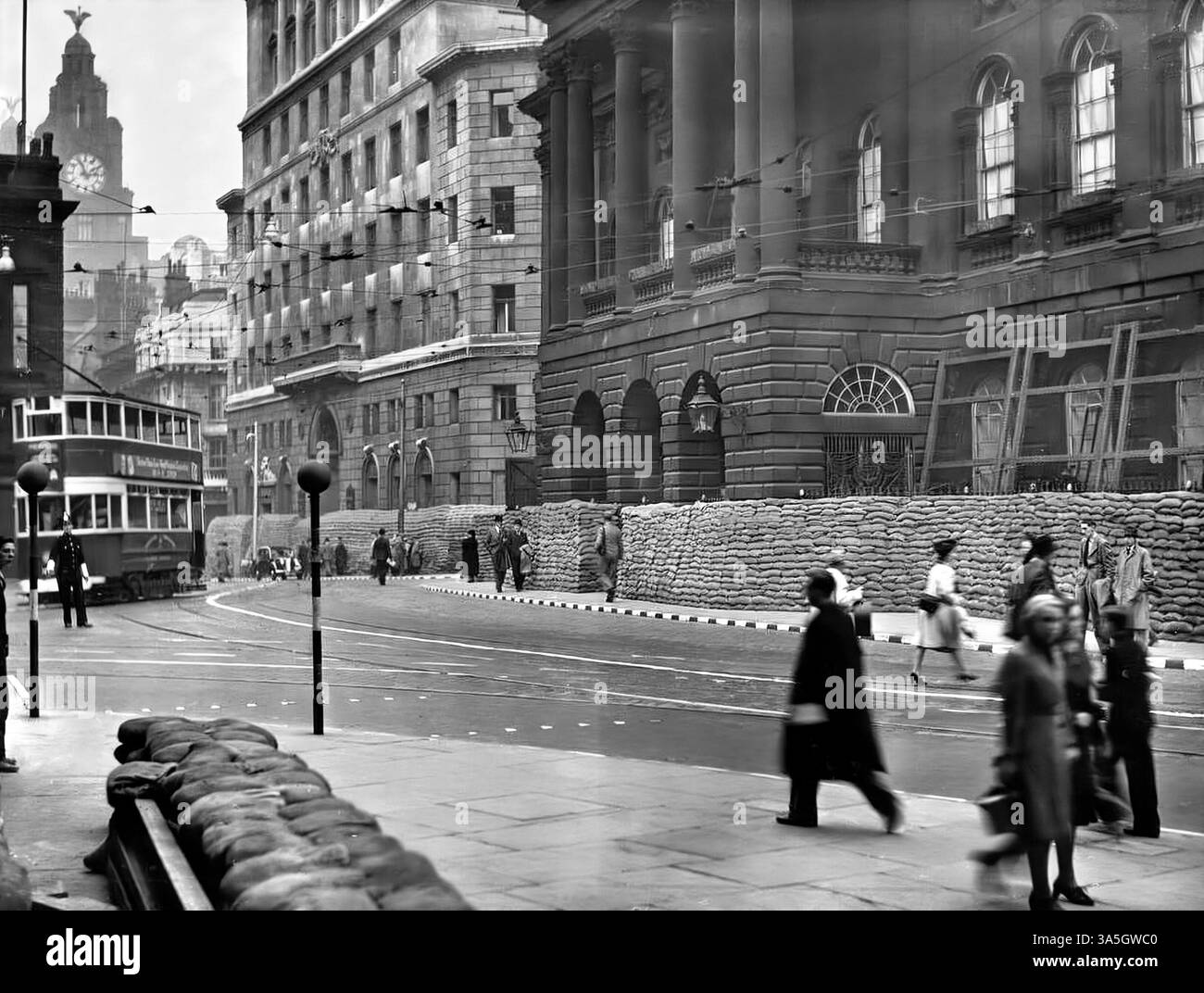 Während des Blitzes des Zweiten Weltkriegs blieb das Leben normal, das Rathaus von Liverpool war von Schutzsandsäcken umgeben. Straßenbahnen fuhren noch, Leute gingen noch zur Arbeit, während man in der Ferne den Liver Bird auf den Lebergebäuden am Ufer sehen kann. Stockfoto