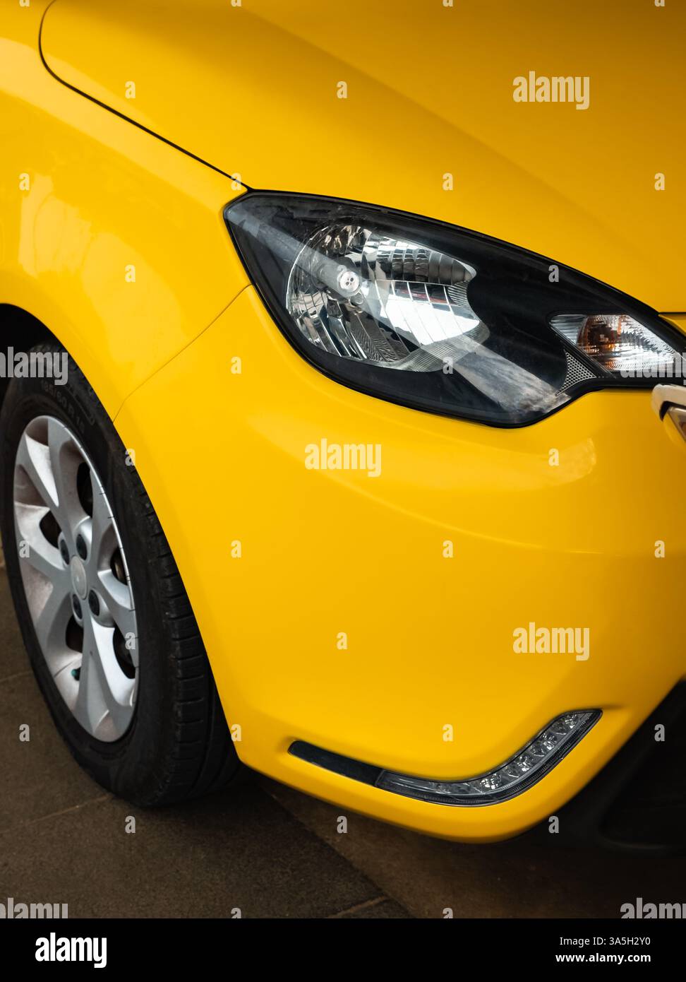Nahaufnahme des Frontscheinwerfers und des Rades eines gelben modernen Autos. Scheinwerfer auf gelbem Auto, Vorderansicht, Nahaufnahme. Scheinwerfer eines Fahrzeugs. Niemand, stree Stockfoto