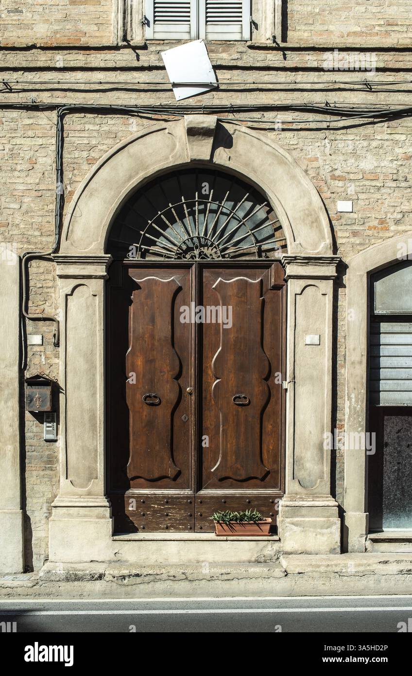 Alte typisch italienische Holztür. Italienisches Haus. Alte Hausfassade. Sonnenlicht. Runder Türlauf. Aus Stein gebautes Haus. Türgriffe aus Schmiedeeisen Stockfoto