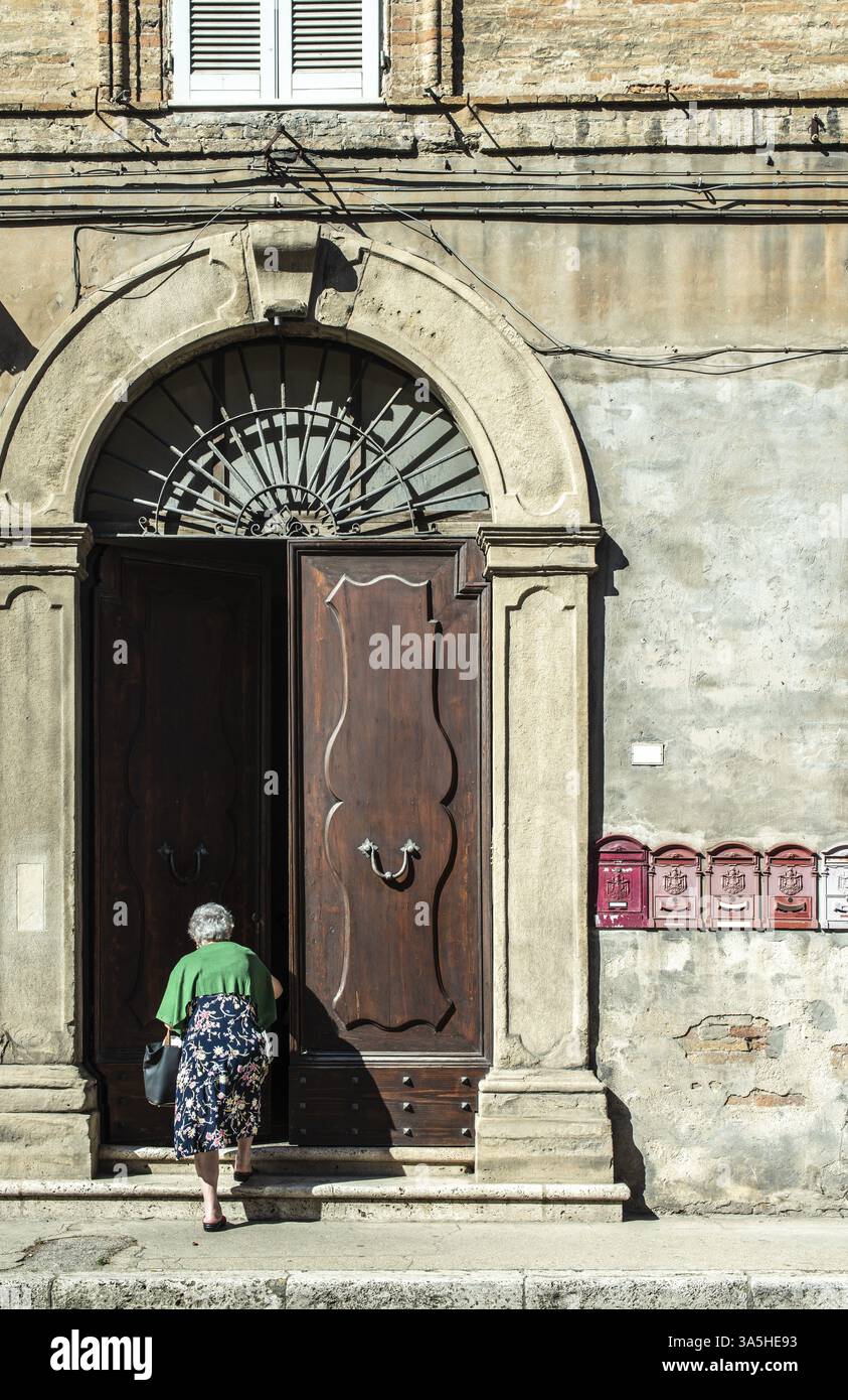Ältere Frau geben Sie im Haus. Alte typisch italienischen Holztür. Italienische Haus. Altes haus Fassade. Sonnenlicht. Runde Tür arch. Steinen bauen Haus. W Stockfoto