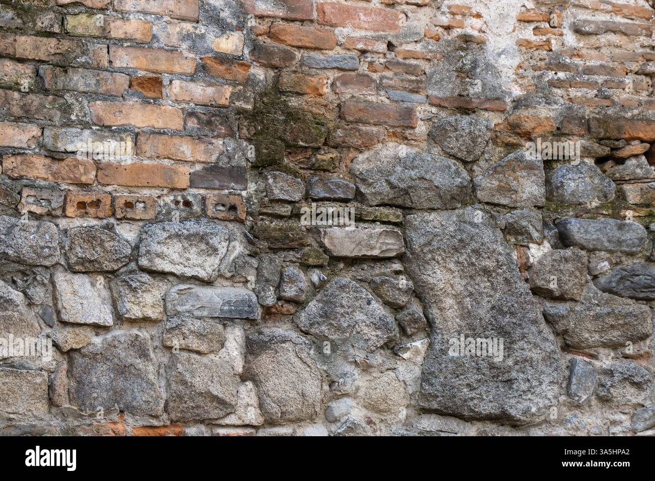Diese faszinierende Wand besteht aus einer Mischung aus alten Ziegeln und zerklüfteten Steinen, die jeweils eine Geschichte von Zeit und Handwerk erzählen. Natur und Geschichte treffen aufeinander Stockfoto