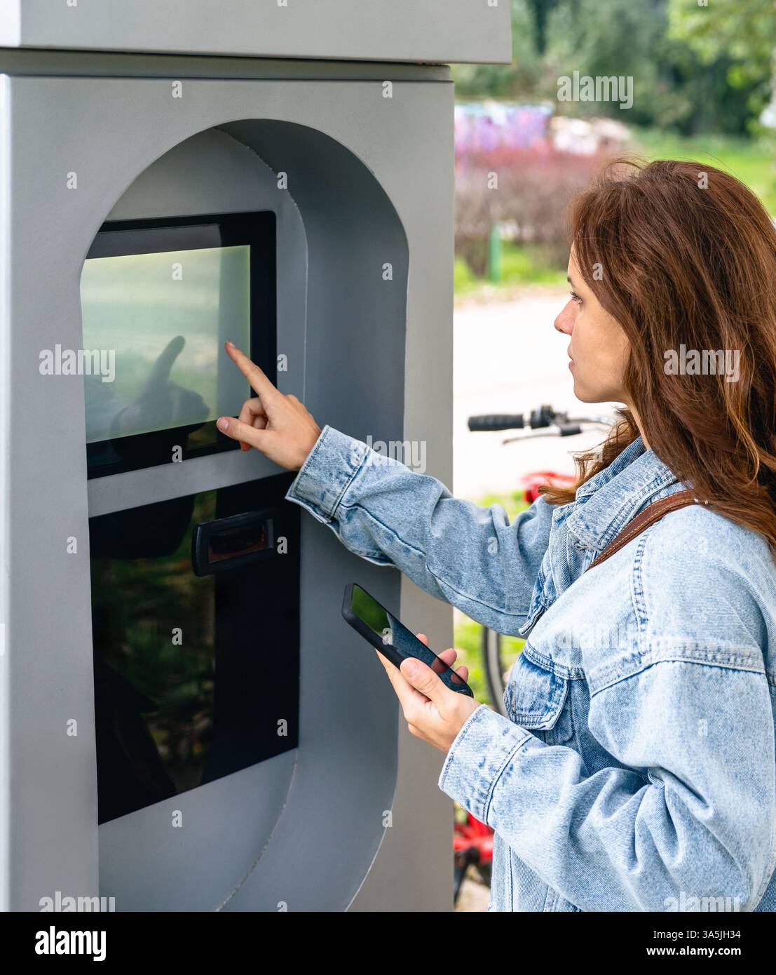 Frau, die den Bildschirm des Selbstbedienungs-Automaten auf der Stadtstraße berührt. Stockfoto
