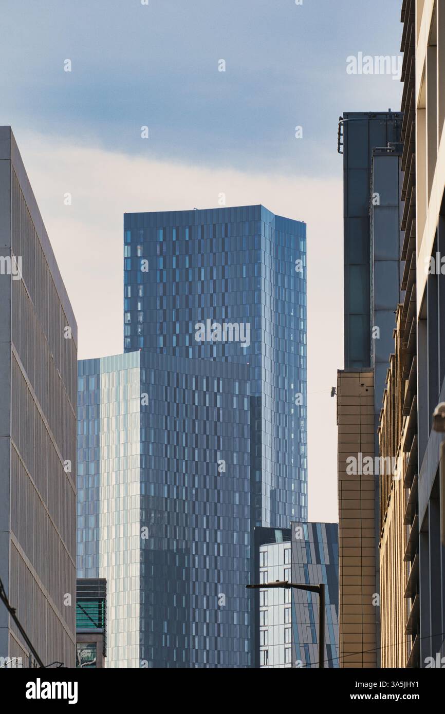 Das Bild zeigt mehrere moderne Gebäude mit unterschiedlicher Höhe und Design vor hellem Himmel. Vorherrschende Farben sind Blau, Grau und einige Bräunungen in Manch Stockfoto
