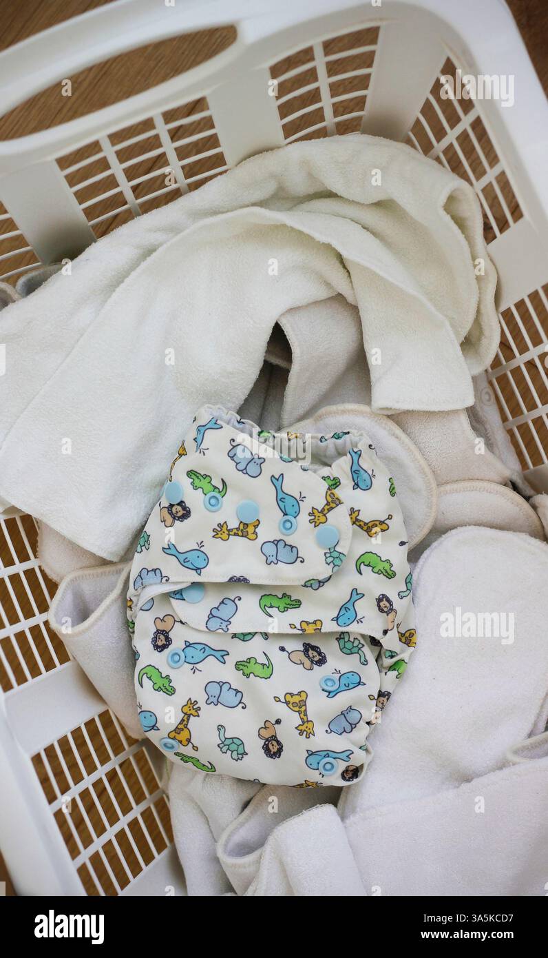 Eine Babywindel aus gemustertem Stoff mit Tierbildern in einem Wäschekorb voller sauberer, weißer, waschbarer Bambus-Babywindeln. Stockfoto
