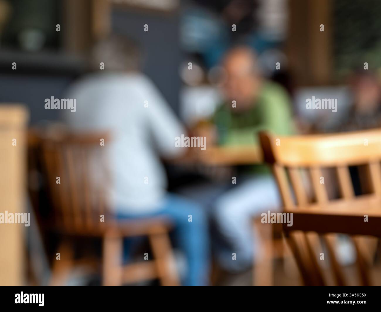 Verschwommenes Foto eines älteren Paares, das an einem Café-Tisch sitzt. Warme Töne und die Unschärfe machen ihn ideal als Hintergrund für Text oder Design Stockfoto