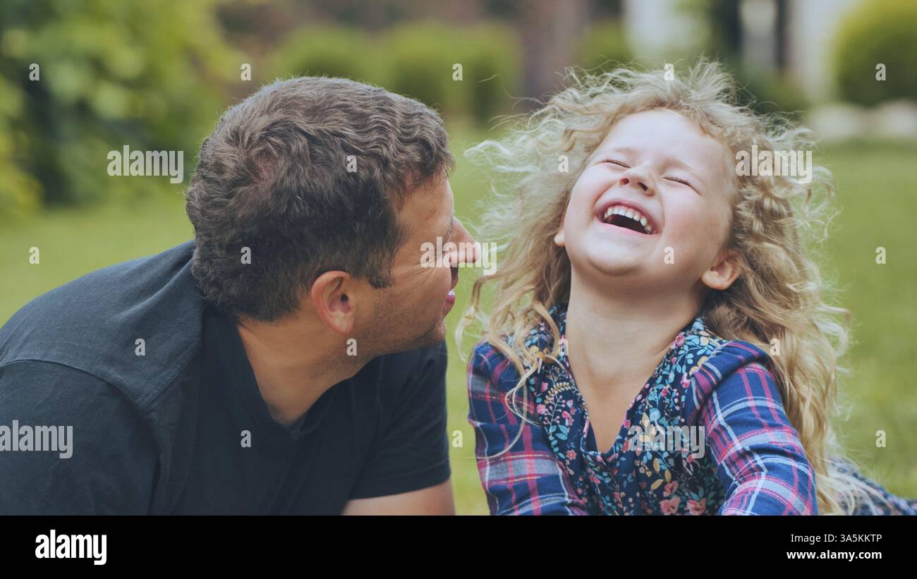 Vater lacht zusammen mit Tochter während des sonnigen Parkspaziergangs und genießt spielerische Bindungsmomente mit echtem Familienglück Stockfoto