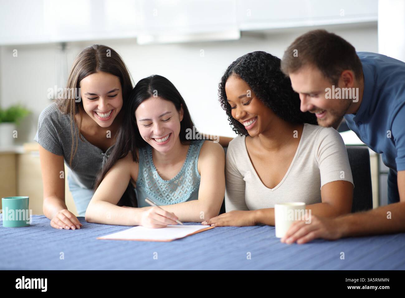 Vier glückliche Mitbewohner, die den Vertrag in der Küche zu Hause überprüfen Stockfoto