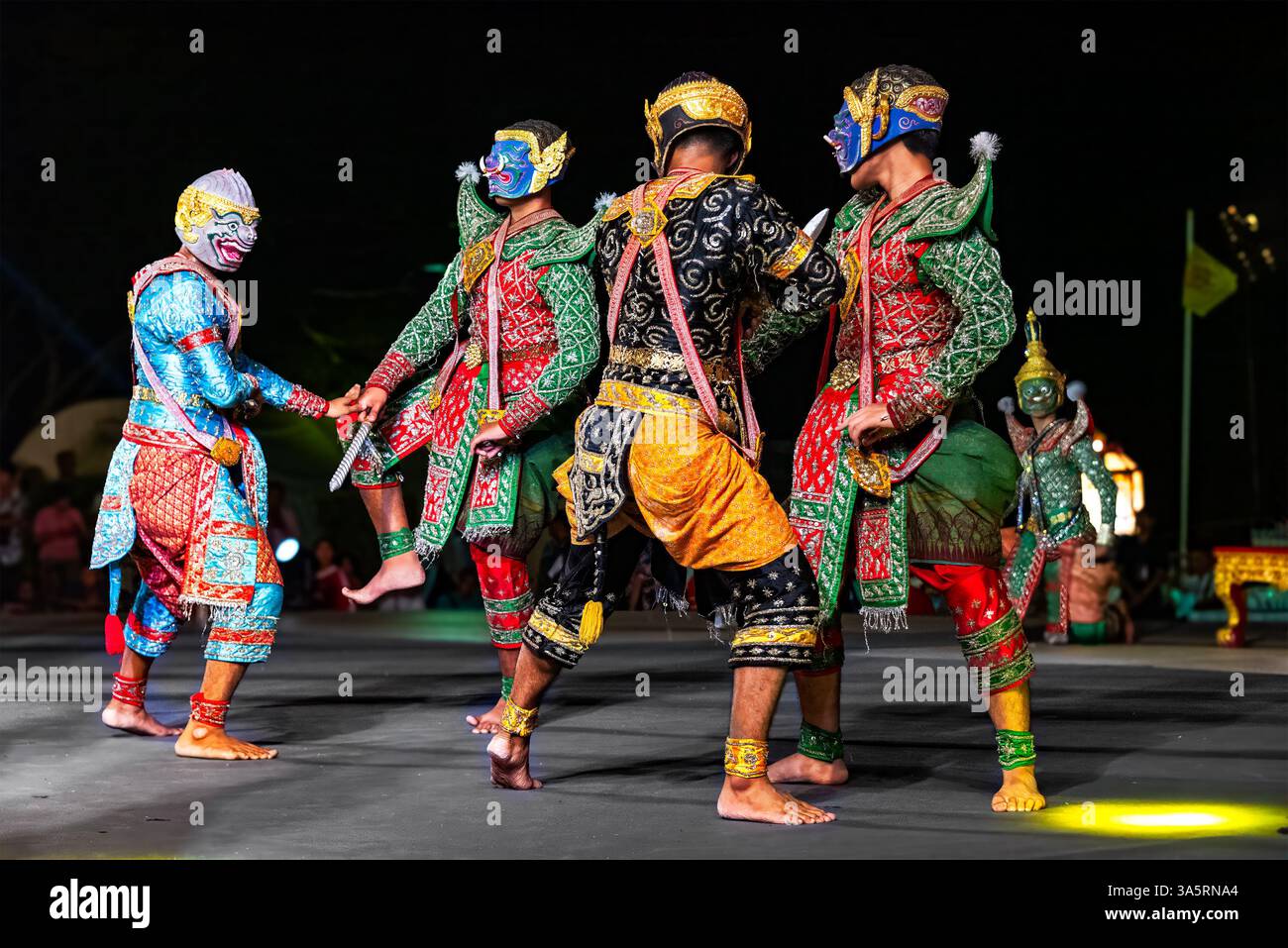 Vier Personen führen nachts auf einer Bühne im Freien ein Tanzdrama-Gen namens „Khon“ auf. Die Tänzer sind in aufwendigen Kostümen verziert. Stockfoto