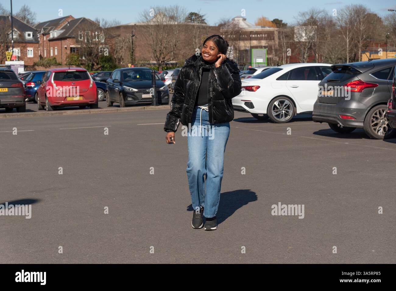 Chichester England Großbritannien. 18.03.2025. Frau in schwarzer Jacke und trägt Jeans, die auf dem Parkplatz laufen. Stockfoto