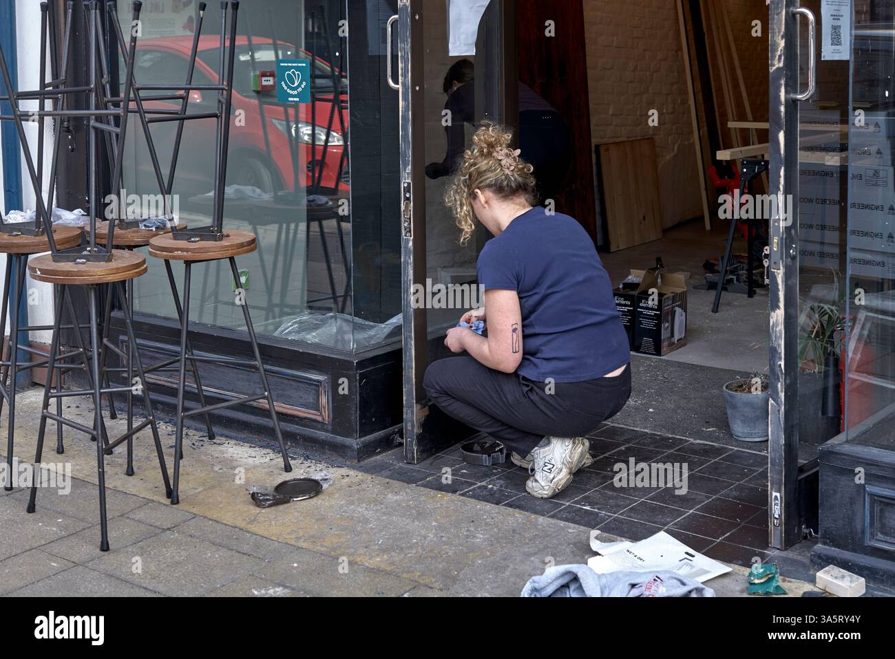 Frau, die draußen arbeitet, malt draußen ein Geschäft. England. Frauen Handarbeit UK Stockfoto
