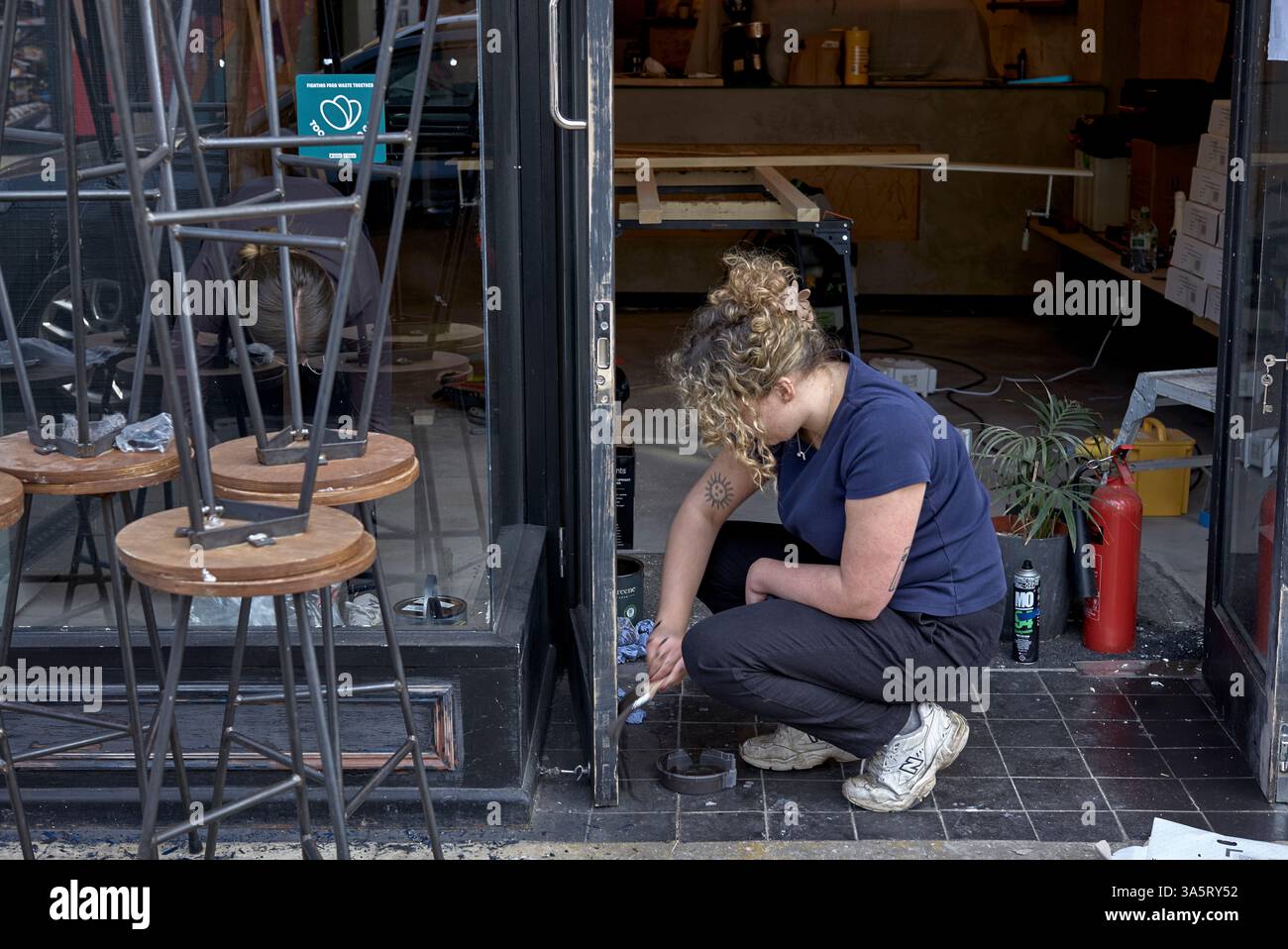 Frau, die draußen arbeitet, malt draußen ein Geschäft. England. Frauen Handarbeit UK Stockfoto
