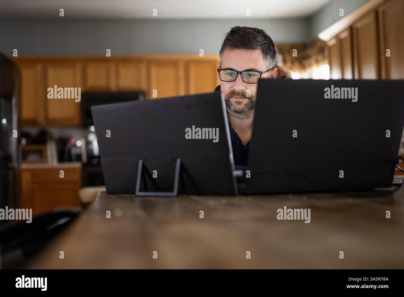 Erwachsener Mann mit Glas, der auf den Computerbildschirm schaut, der von zu Hause aus arbeitet Stockfoto