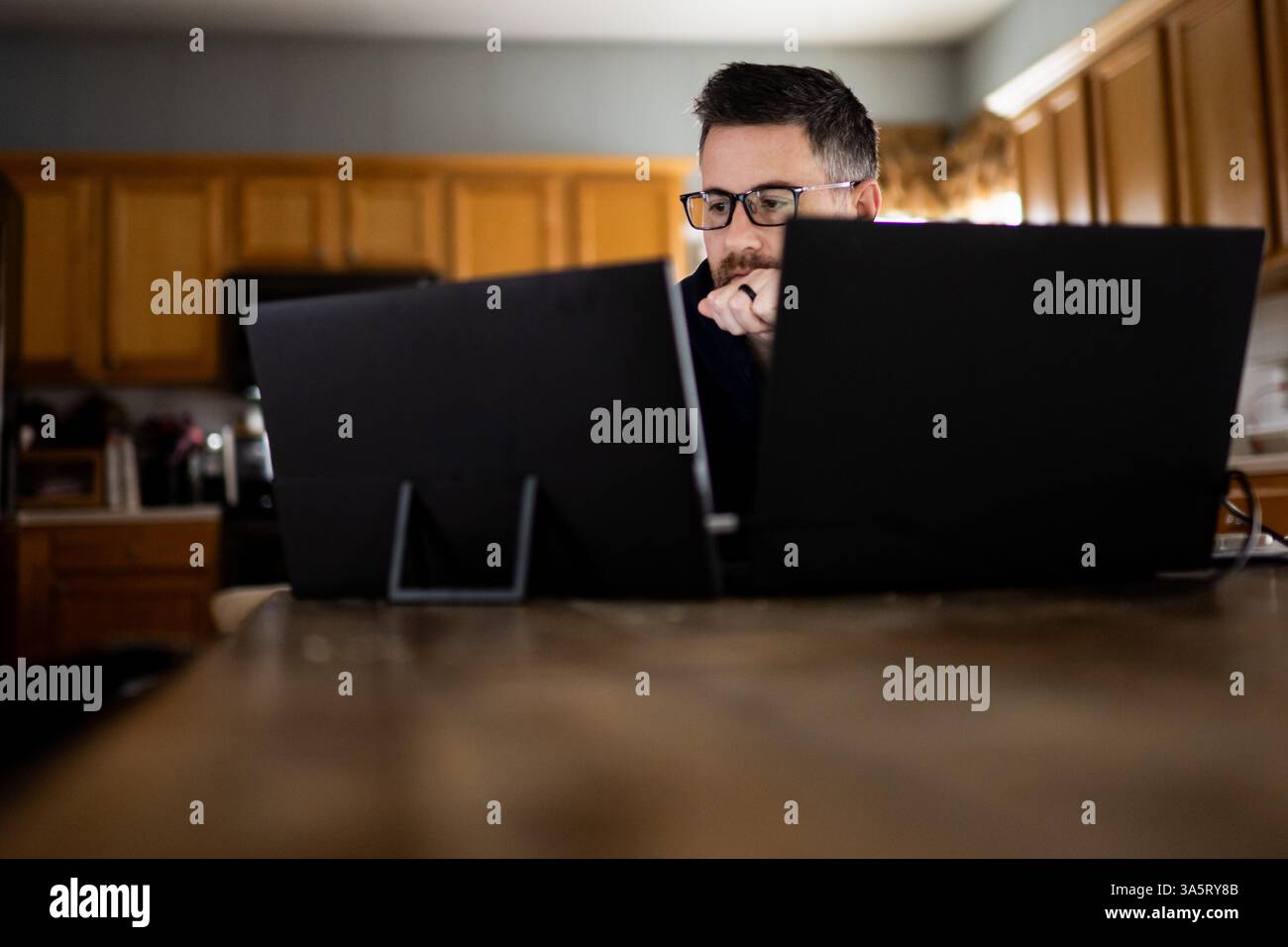 Erwachsener Mann mit Brille, der von zu Hause aus auf einen Laptop schaut Stockfoto