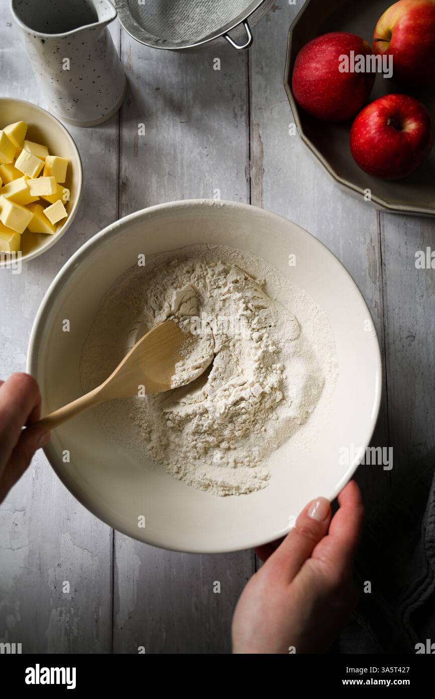 Hausbackkonzept. Eine Schüssel mit weißem Mehl, Äpfeln und Butter Stockfoto