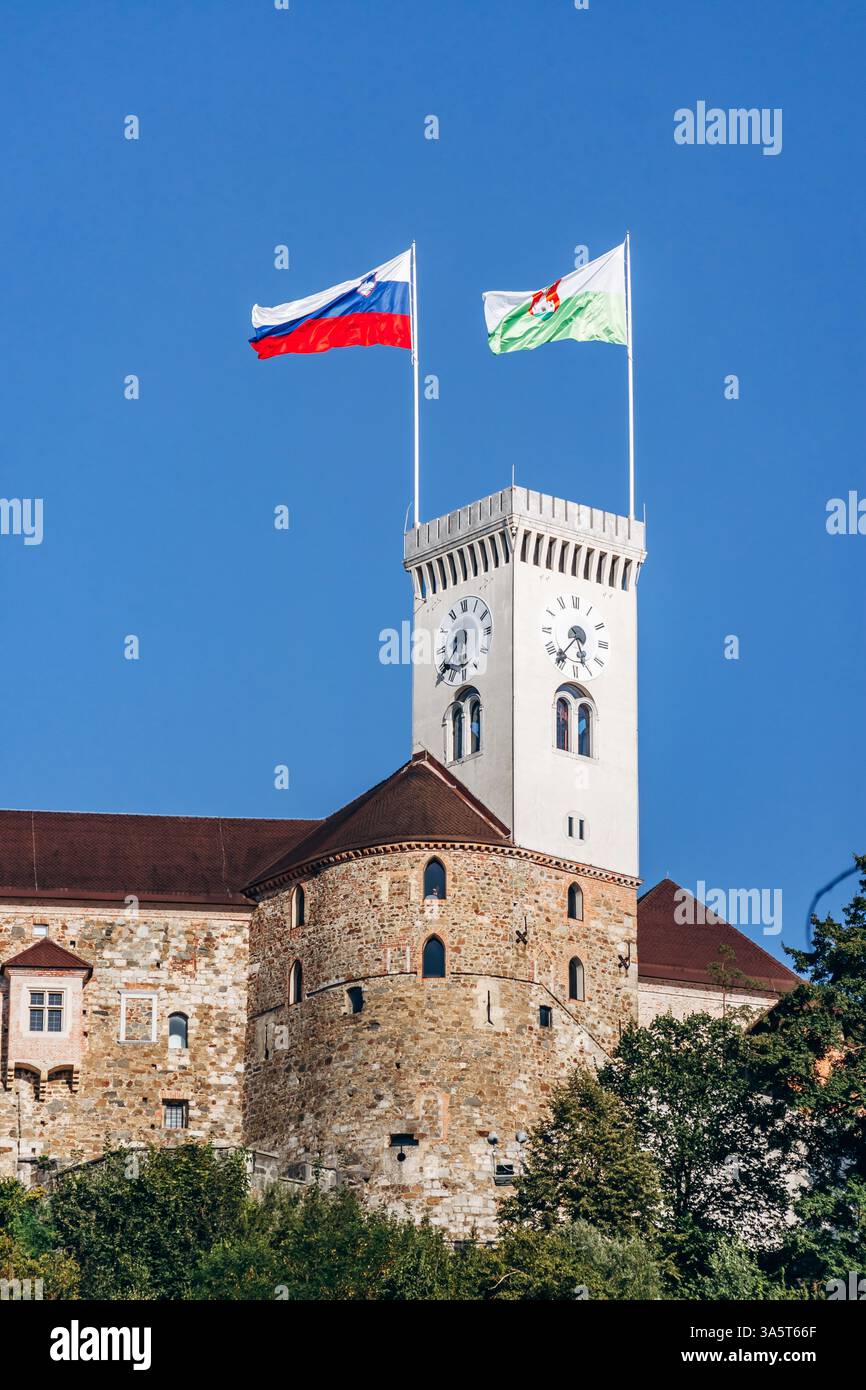 Ljubljana, Slowenien - 15. August 2024: Burg von Ljubljana mit slowenischen Flaggen und Stadtflaggen, die auf dem Turm schwenken und die historische Stadt überblicken Stockfoto