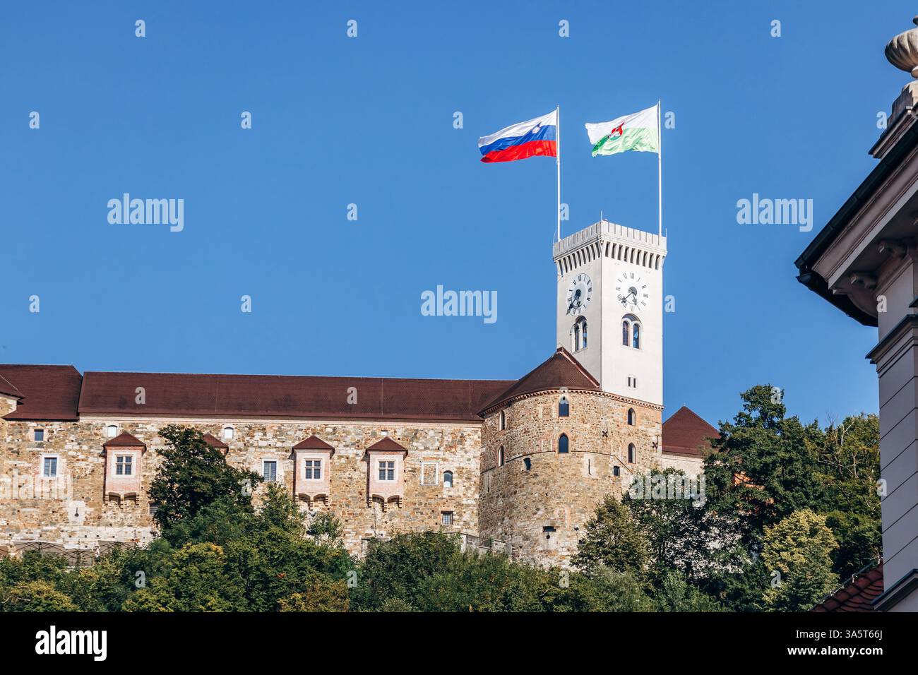 Ljubljana, Slowenien - 15. August 2024: Burg von Ljubljana mit slowenischen Flaggen und Stadtflaggen, die auf dem Turm schwenken und die historische Stadt überblicken Stockfoto