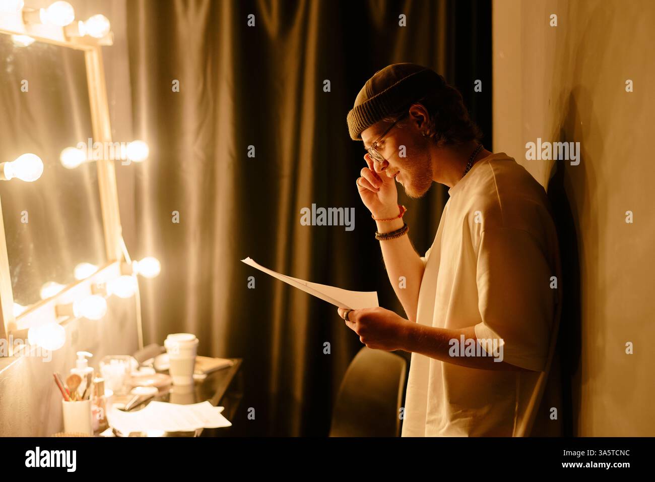 Einzelne stehen hinter der Bühne und halten das Skript neben dem beleuchteten Spiegel, das über die bevorstehende Vorstellung reflektiert. In letzter Minute werden die Vorbereitungen für die nächste Szene leise einstudiert Stockfoto