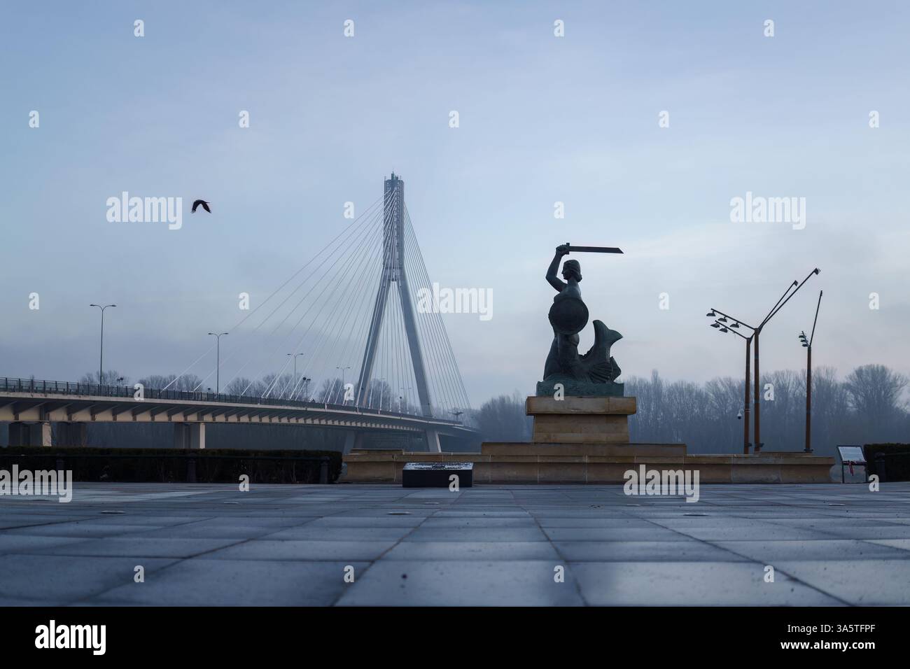 Warschau, Polen. 27. Januar 2025 - Meerjungfrauenstatue mit Swietokrzyski-Brücke im Hintergrund, am frühen Morgen. Stockfoto