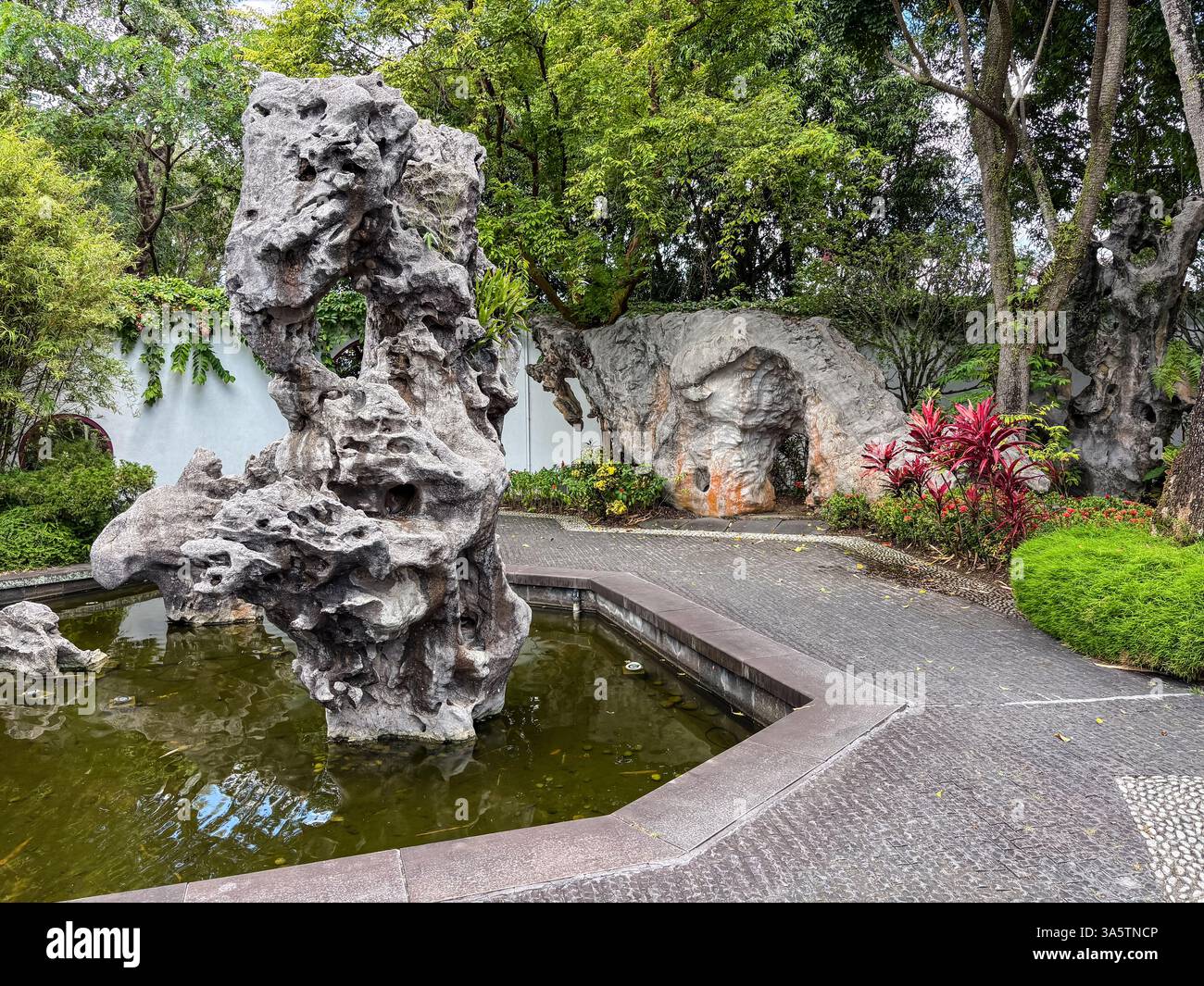Der Chinesische Garten in Singapur zeigt einen Felsblock, der eine natürliche Landschaft mit grauen Felsen, grünen Bäumen, Pflanzen und einem Teich nachahmt. Stockfoto