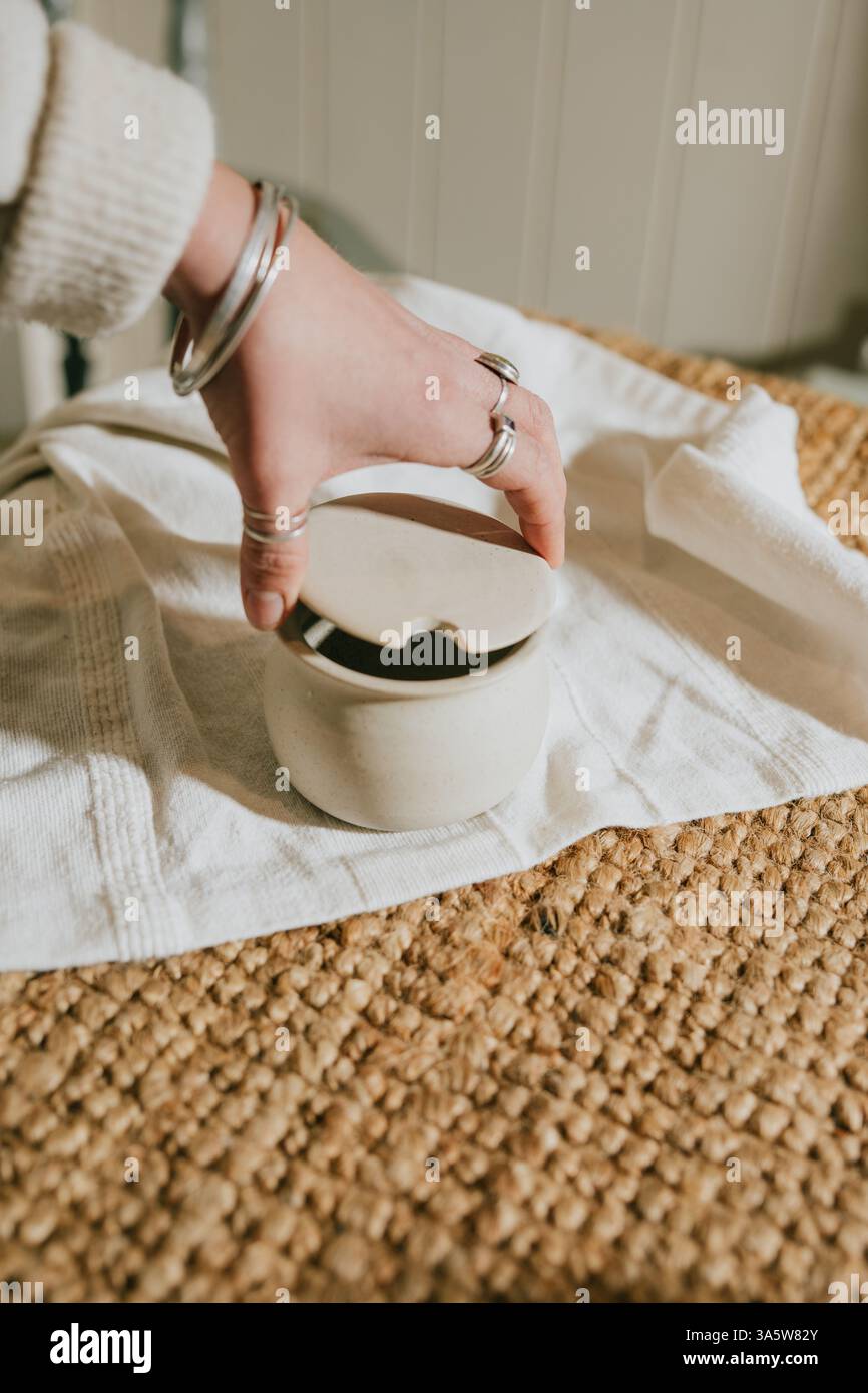 Eine Frau hält ein weißes Keramikglas mit Deckel auf einem Teppich. Der Becher wird wahrscheinlich zur Aufbewahrung oder Aufbewahrung von Dingen wie Gewürzen oder kleinen Gegenständen verwendet. Th Stockfoto